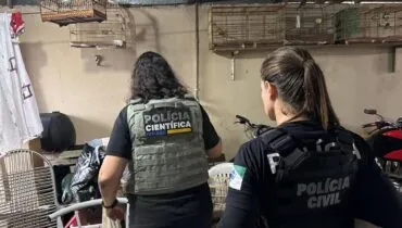 Imagem mostra duas policiais civis em uma casa com gaiolas ao fundo