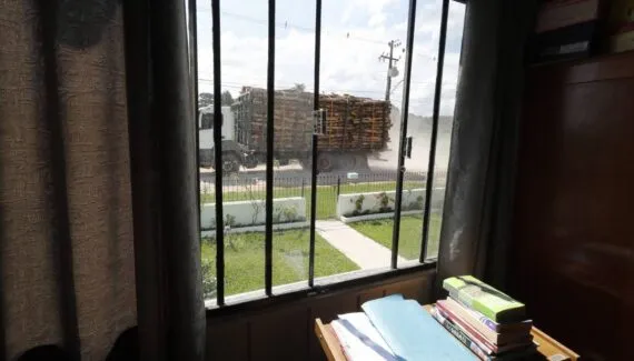 Imagem mostra a janela de uma casa em uma rua de saibro, cheia de poeira de um caminhão passando