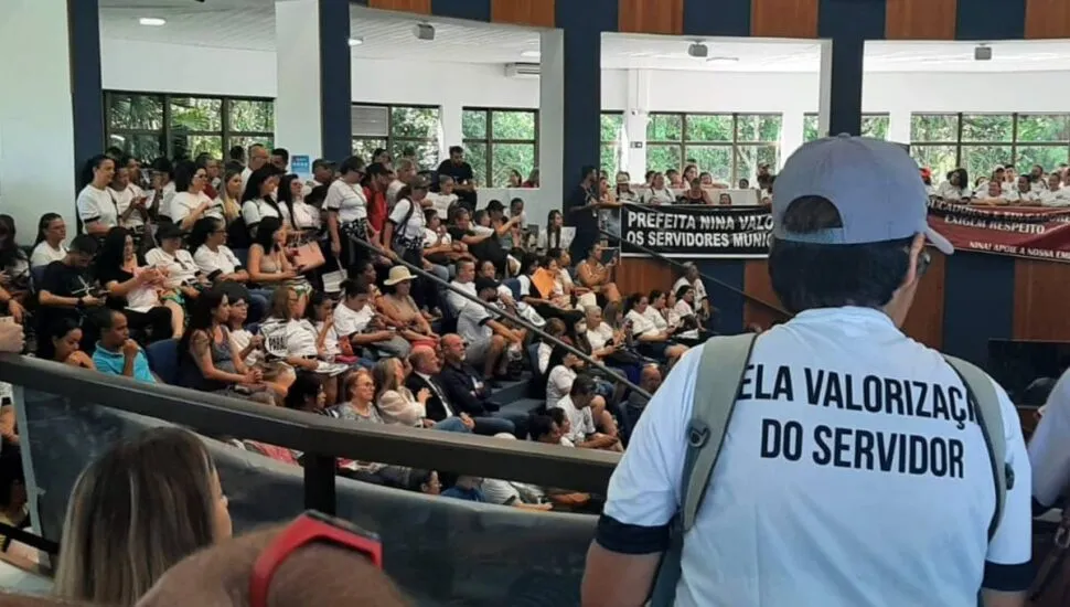 Imagem mostra a câmara de São José dos Pinhais lotada de servidores. No detalhe, uma trabalhadora veste uma camiseta branca com o dizer "Pela valorização do servidor"
