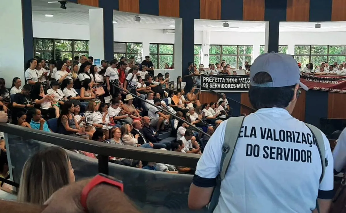 Imagem mostra a câmara de São José dos Pinhais lotada de servidores. No detalhe, uma trabalhadora veste uma camiseta branca com o dizer "Pela valorização do servidor"