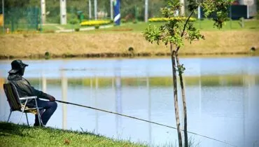 Imagem mostra um homem pescando em um parque de pinhais num dia de muito calor