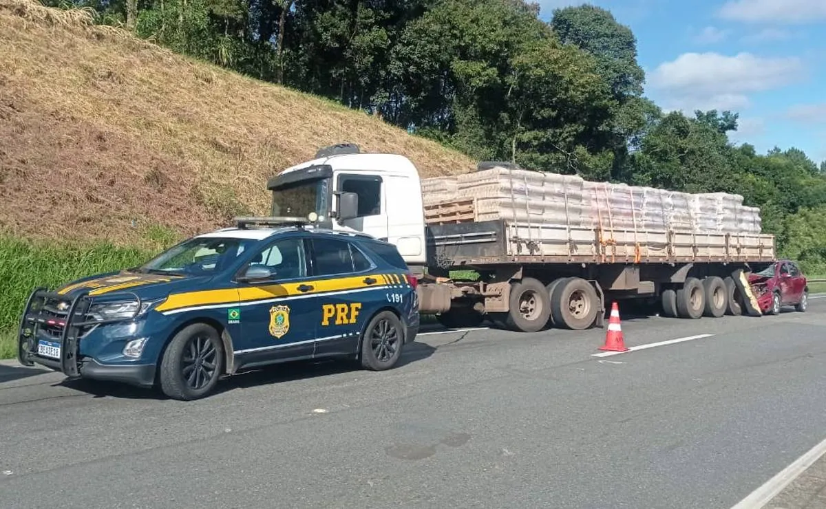 imagem mostra uma viatura da PRF com um caminhão e um carro acidentado ao fundo