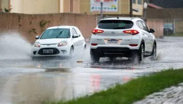 Imagem mostra dois carros passando em um trecho alagado de Curitiba.