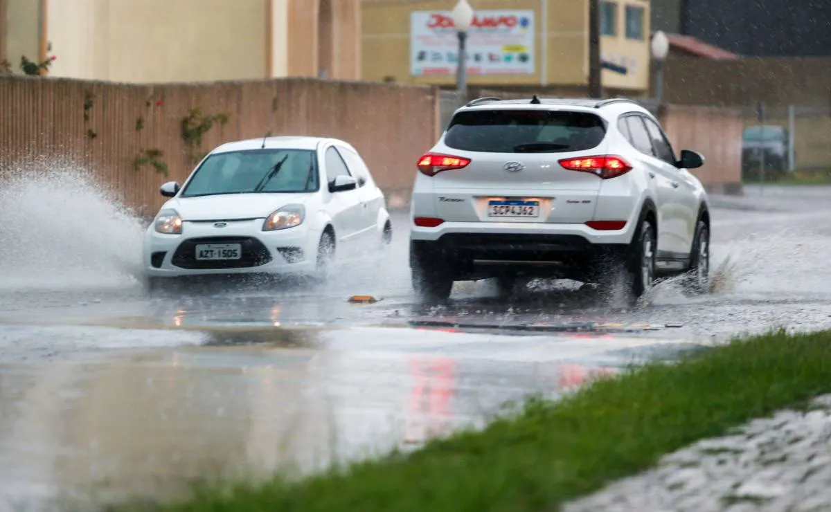 Imagem mostra dois carros passando em um trecho alagado de Curitiba.