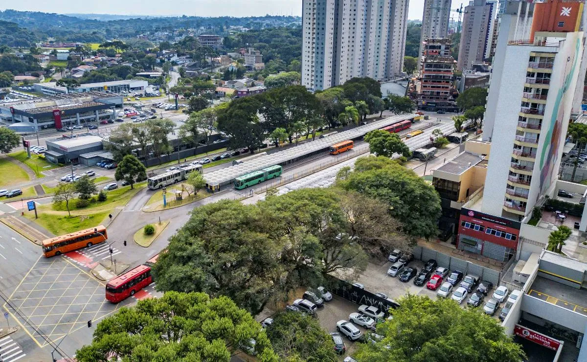 Imagem aérea mostra o novo smart park de Curitiba. A imagem de prédios, um terminal com ônibus e muitas árvores.