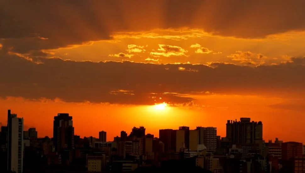 Imagem mostra nuvens iluminadas pelo sol, num fim de tarde em Curitiba. A imagem tem predominância da cor laranja com a silhueta de prédios.