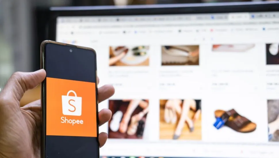 Na imagem, um celular com o logotipo da Shopee em frente a um computador com o site do e-commerce aberto.