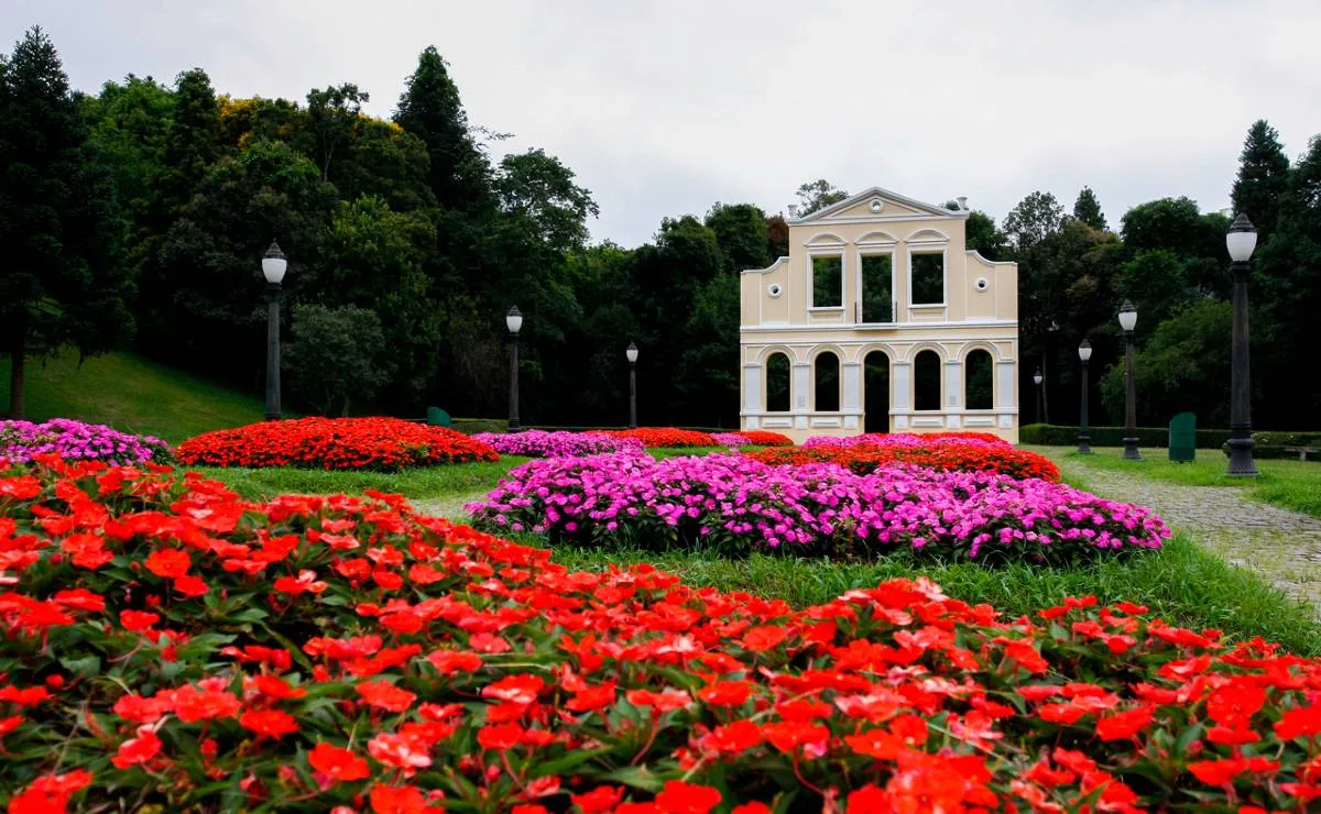 Imagem mostra o Bosque do Alemão com uma estrutura em alvenaria e flores vermelhas e rosas.