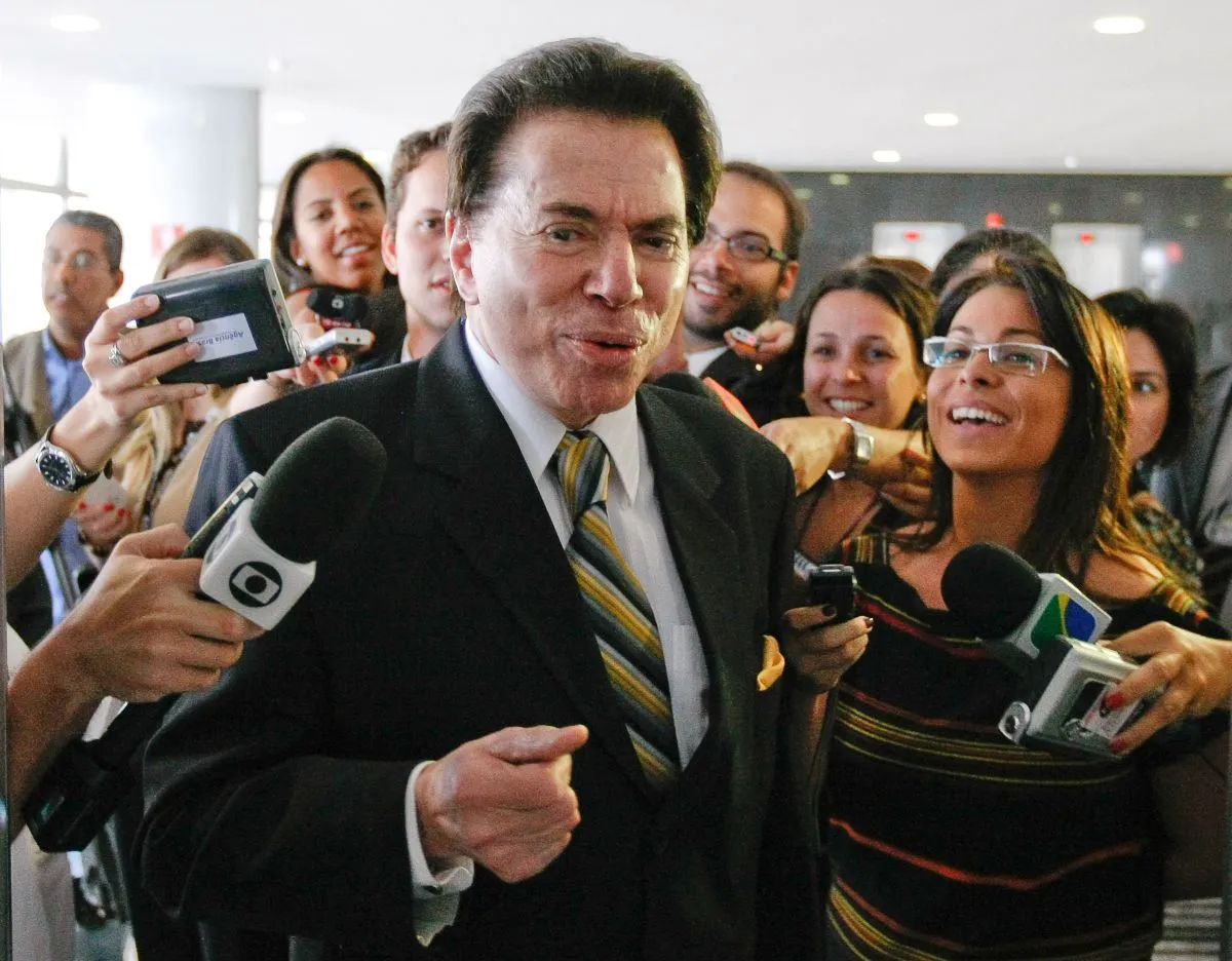 Na foto, Silvio Santos dá entrevista rodeada por muitos repórteres e vários admiradores, todos sorrindo