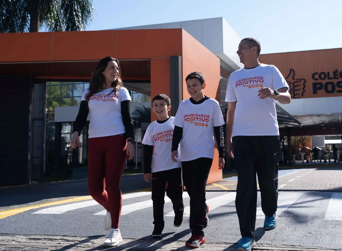 Imagem mostra uma mãe, dois meninos e um pai, todos com a camiseta da Caminhada Positivo, em frente ao colégio