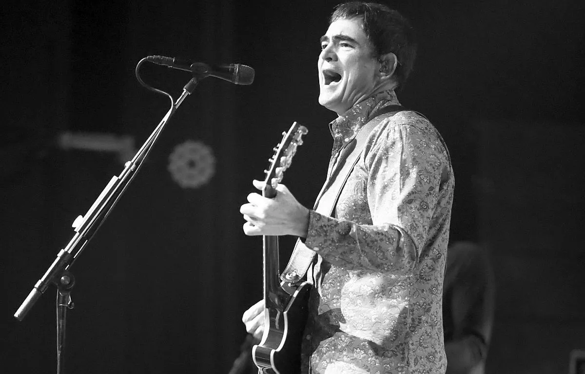 Foto mostra cantor samuel rosa tocando uma guitarra e cantando em um microfone num pedestal