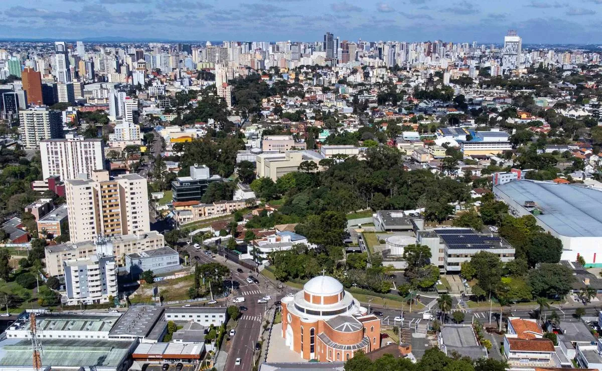 Imagem mostra Curitiba vista de cima, com muitas árvores e prédios baixos.