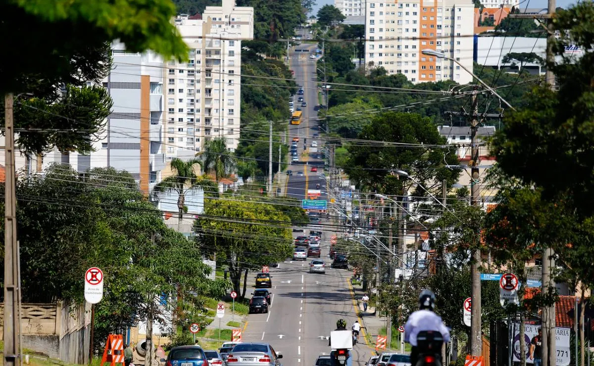 Imagem mostra uma avenida de Curitiba com muitas árvores e pessoas circulando.