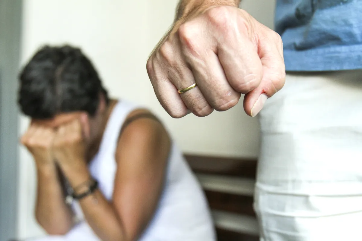 Na imagem, uma mulher aparece ao fundo, acuada e cobrindo os olhos. E também há um homem com a mão fechada, em uma simulação de violência contra a mulher.