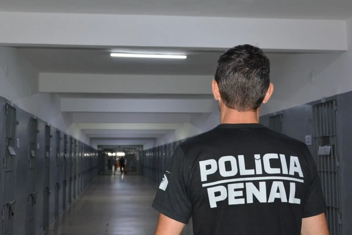 Na imagem, um agente da polícia penal em um corredor entre as celas, dentro de um presídio.