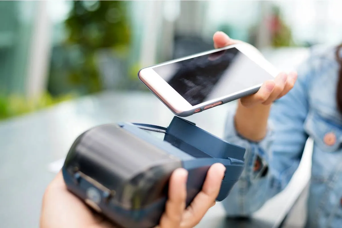 Imagem mostra uma pessoa pagando algo com o celular em uma máquina de cartão.