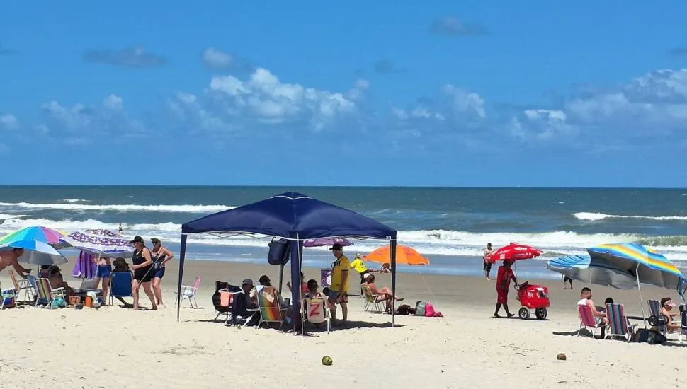 Imagem mostra veranistas curtindo uma praia com calor e céu azul.