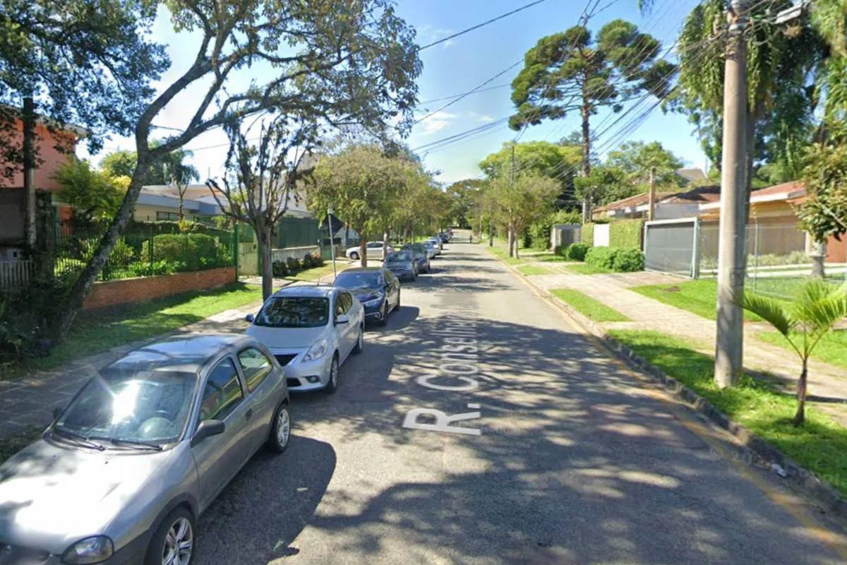 Imagem mostra uma rua de Curitiba em um dia de sol com carros estacionados no lado esquerdo.