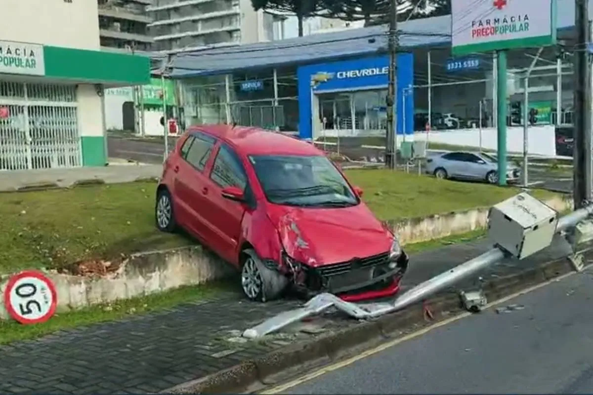 Imagem mostra um acidente em Curitiba. Um carro vermelho está com a frente amassada em cima de um canteiro lateral.