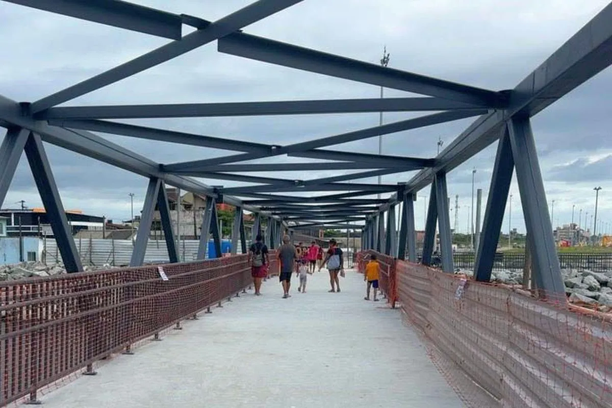 Na imagem, pedestres caminham na nova passarela sobre o Rio Matinhos, no Litoral do Paraná.