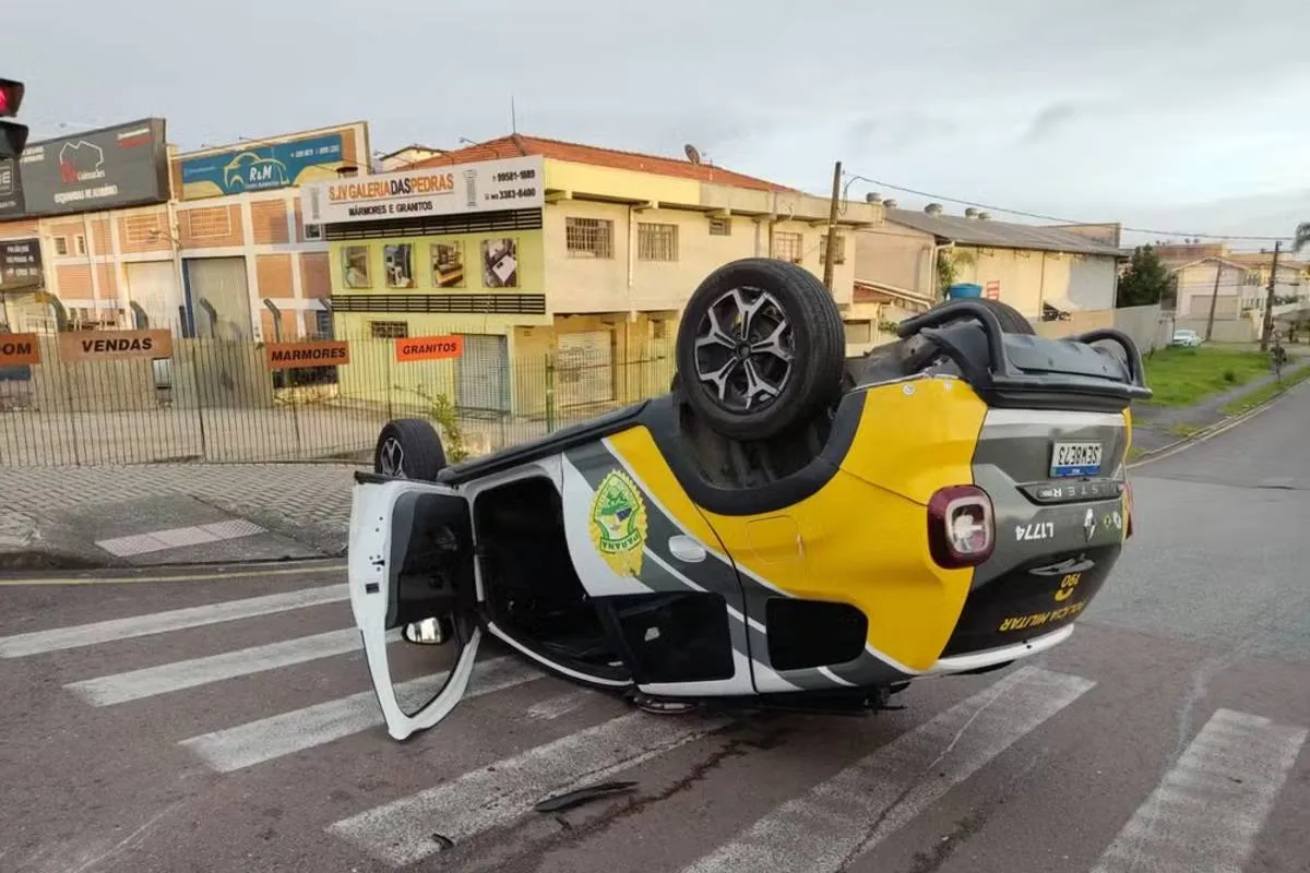 Imagem mostra uma viatura capotada no meio da rua.