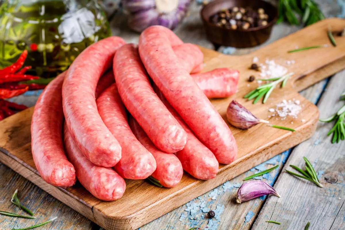 Imagem mostra uma linguicinha de churras em uma tábua com temperos.