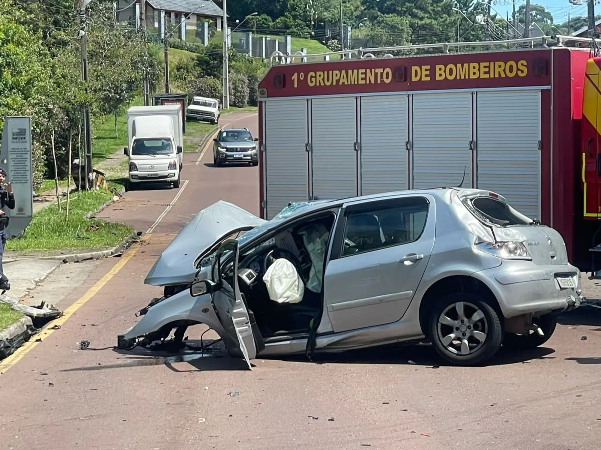 Na imagem, carro com a frente destruída após batida em avenida. Atrás dele, caminhão dos bombeiros.