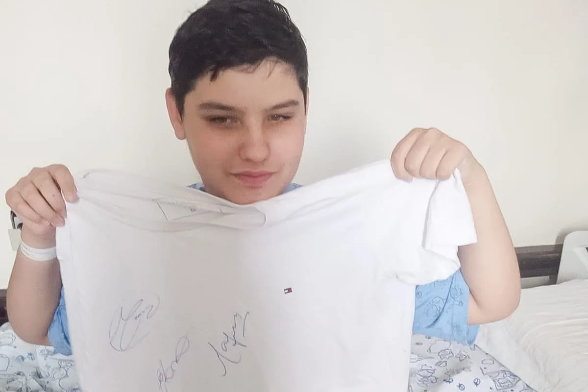 Na imagem, menino Benjamin segurando uma camiseta branca