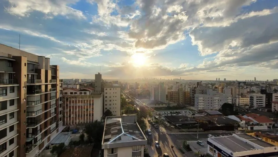 Imagem mostra o por do sol em Curitiba, com muitas nuvens e prédios na região do bairro Vila Izabel.