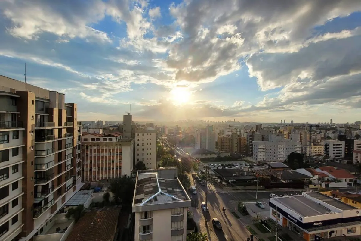 Imagem mostra o por do sol em Curitiba, com muitas nuvens e prédios na região do bairro Vila Izabel.