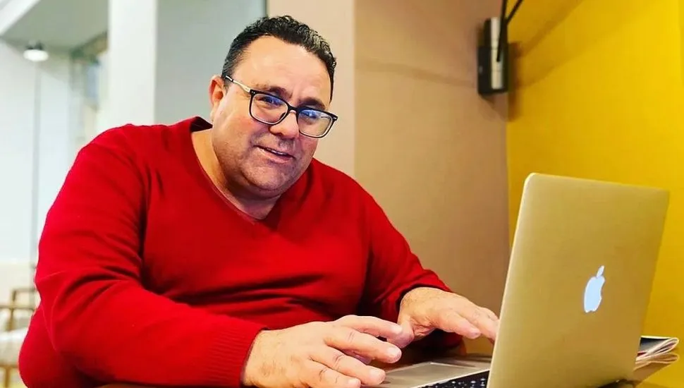 Imagem mostra um homem com uma blusa vermelha utilizando um notebook