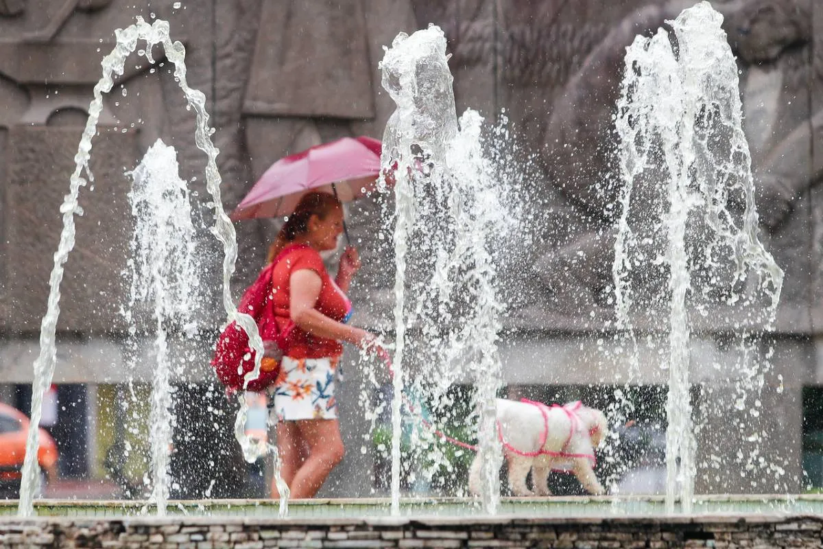Imagem mostra uma mulher em Curitiba com um guarda chuva passando por trás de um chafariz