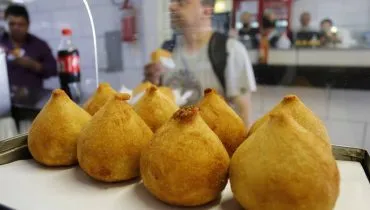 Imagem mostra uma estufa de salgados com várias coxinhas perfeitamente alinhadas.