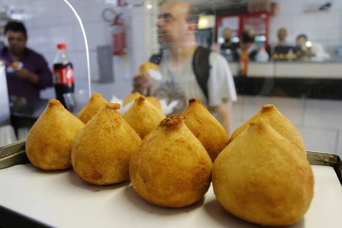 Imagem mostra uma estufa de salgados com várias coxinhas perfeitamente alinhadas.