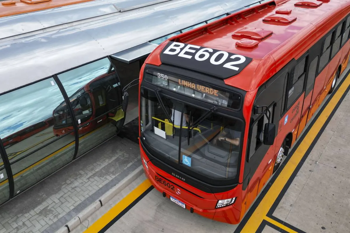 Imagem mostra um ônibus biarticulado vermelho, clássico de Curitiba.