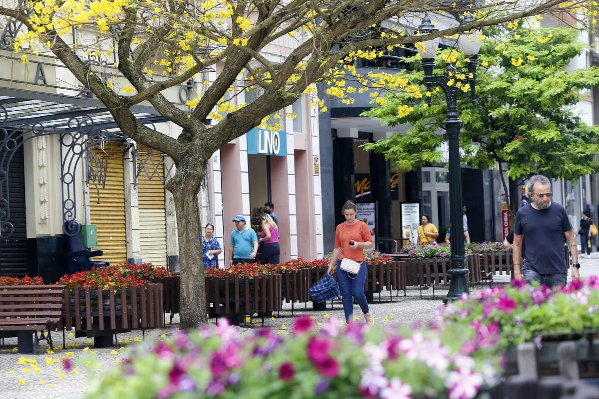 Imagem mostra o Centro de Curitiba com lojas abertas e outras fechadas. Tem pessoas passando com sacolas nas mãos.