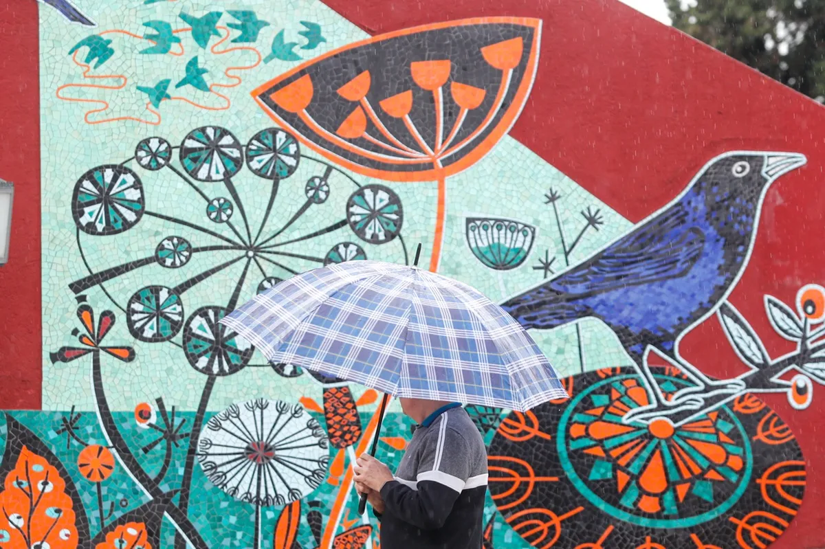 Imagem mostra homem com sombrinha passando por muro pintado em Curitiba