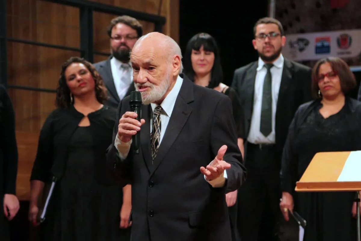 Imagem mostra um homem de terno, com barba e cabelo branco. falando ao microfone.