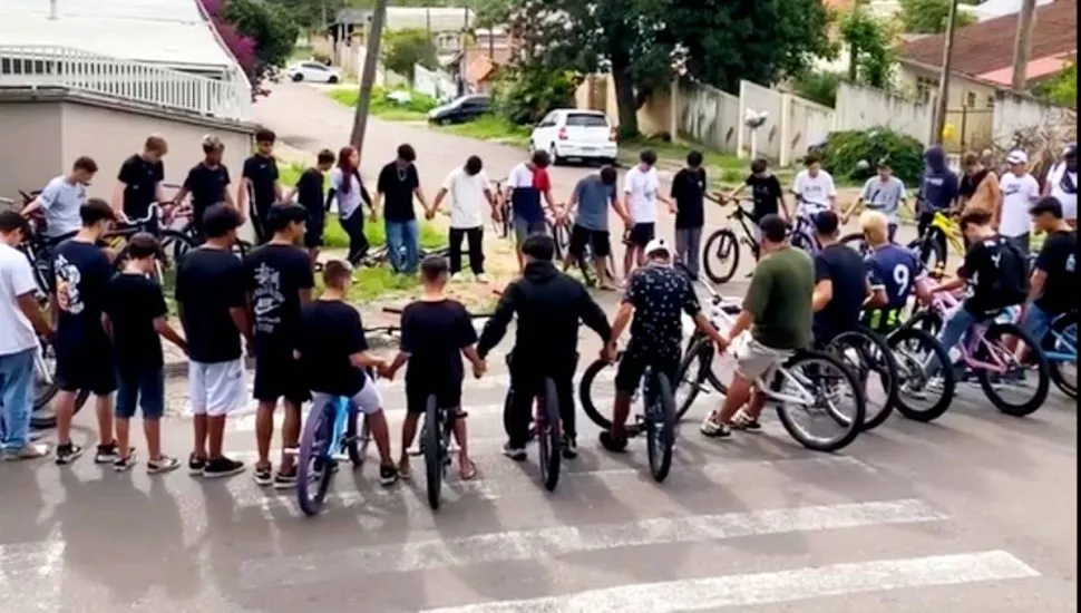 Imagem mostra ciclistas formando um grande círculo, de mãos dadas, fazendo uma oração.