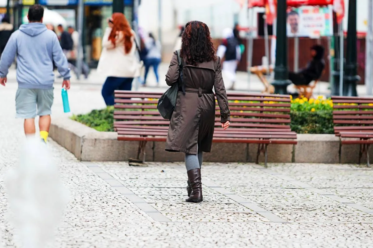Imagem mostra uma mulher com um sobretudo marrom em um dia de frio num calcadão de Curitiba.