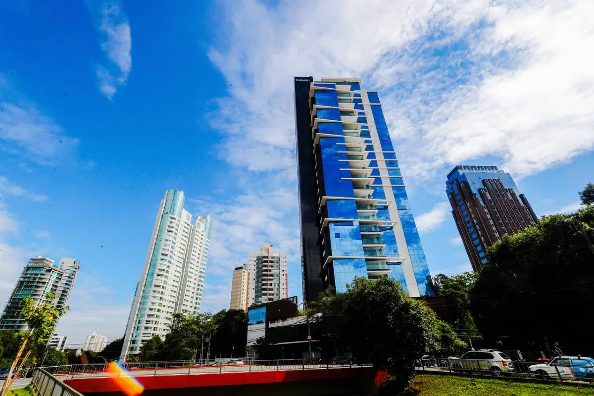 Imagem mostra um prédio de Curitiba com céu azul entre nuvens.