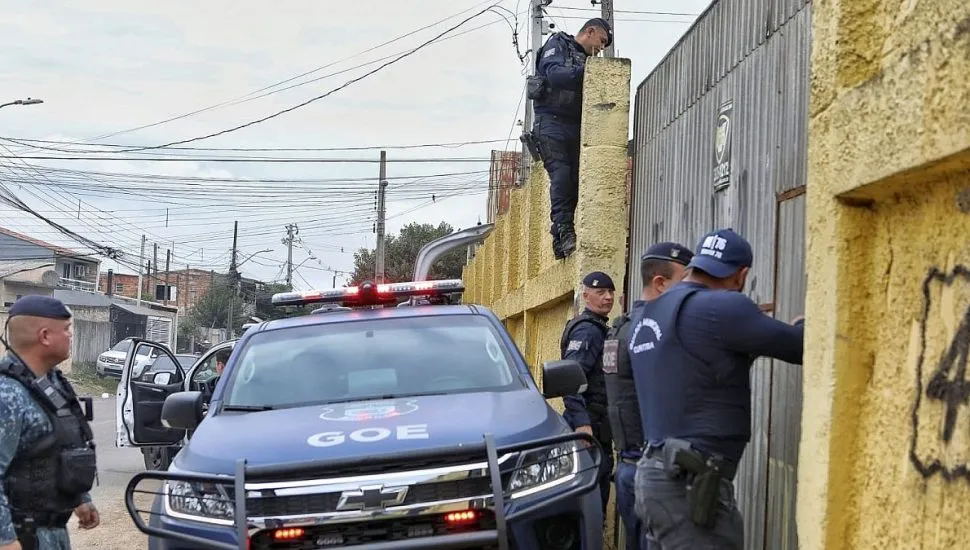 Imagme mostra uma viatura da Guarda Municipal em primeiro plano, com pelo menos 4 guardas, um deles trepado no muro de uma residência