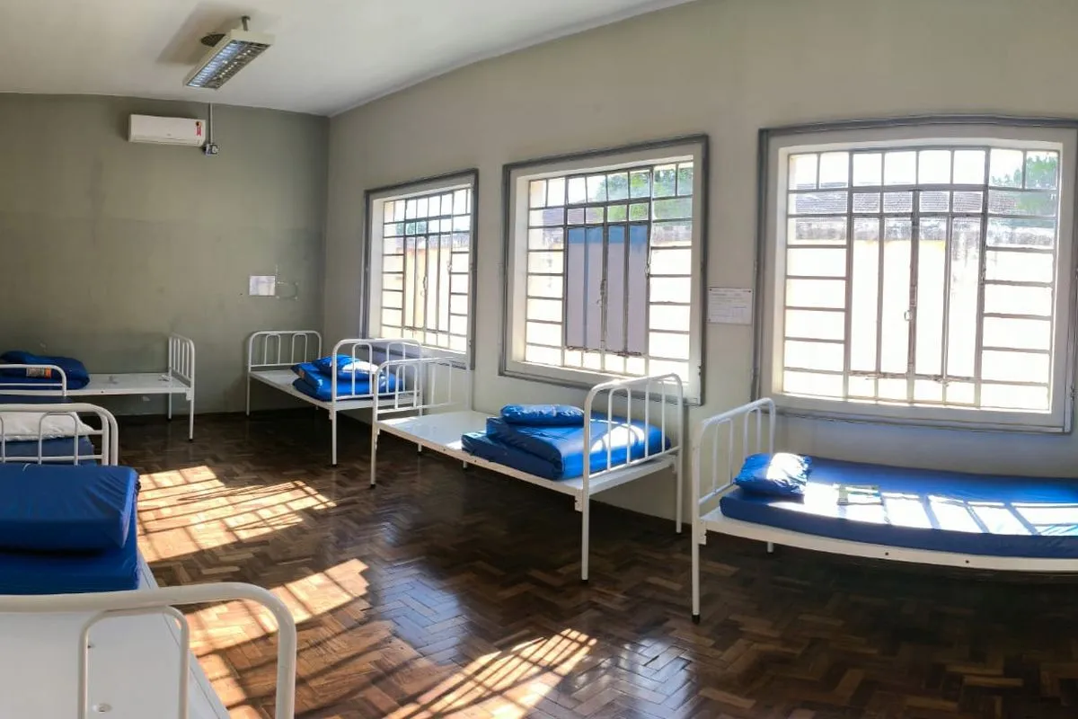 Imagem mostra seis macas dispostas em um salão grande, com três janelas bem iluminadas pela luz do sol