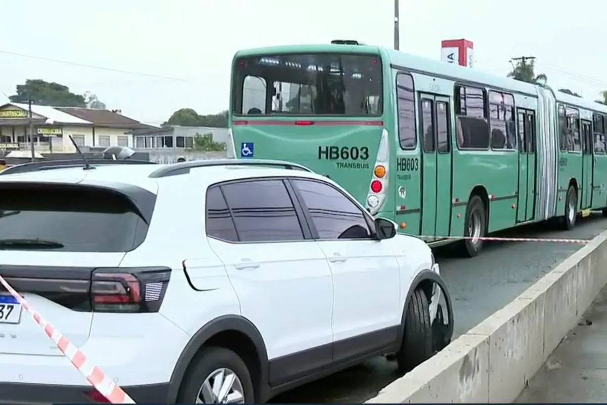 Imagem mostra um carro branco batido ao lado de um ônibus em Curitiba.