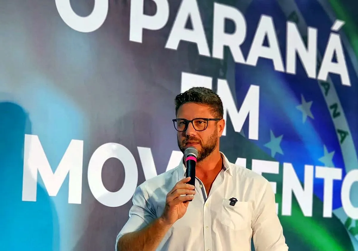 Imagem mostra o deputado Requião Filho segurando um microfone, em frente a um letreiro que diz: Paraná em Movimento