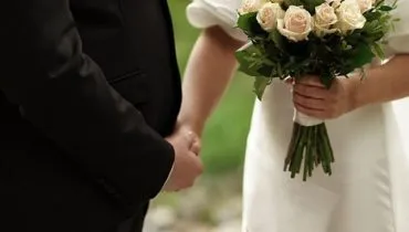 Newlyweds hold hands during a walk in the park.