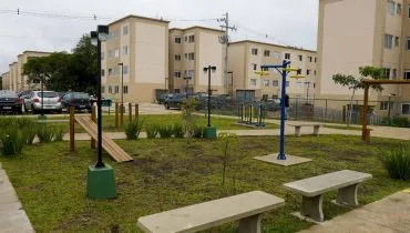 Imagem mostra um prédio da Cohab em Curitiba com céu nublado e um parquinho.