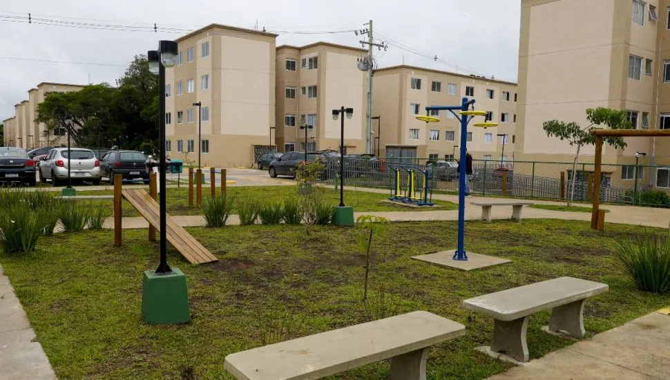 Imagem mostra um prédio da Cohab em Curitiba com céu nublado e um parquinho.