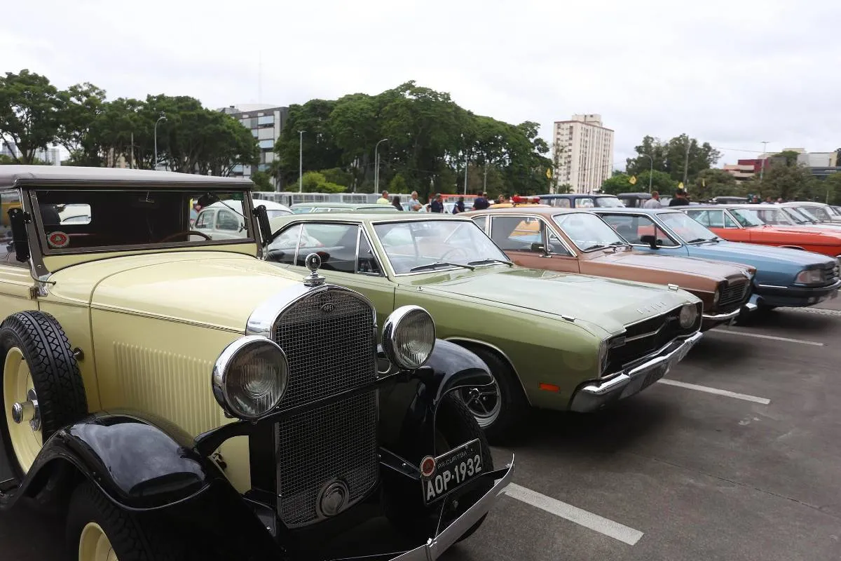 Imagem mostra carros antigos em um estacionamento. São veículos clássicos com placa preta.