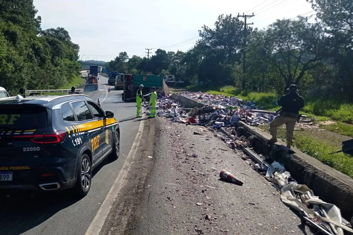 Imagem mostra um cenário de acidente na BR-116. Com uma viatura da PRF e muita carga espalhada no chão.